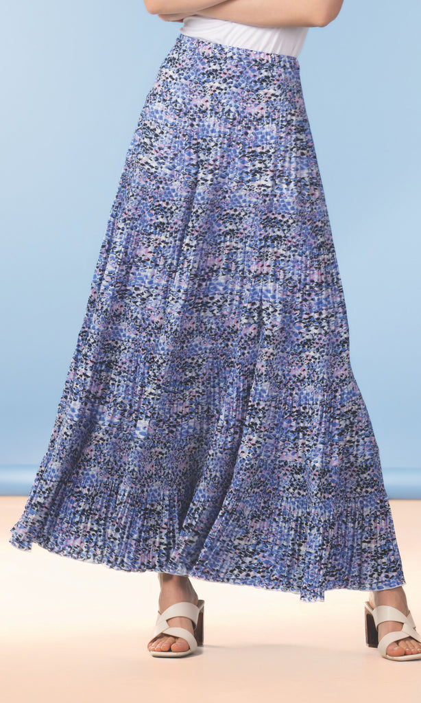 Person wearing a blue floral skirt on a beach with a clear blue sky.