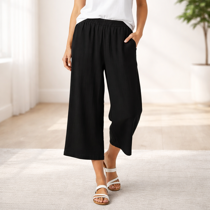 Woman wearing a white t-shirt and black wide-leg pants in a bright room.