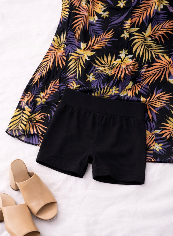 Black shorts with a colorful floral-patterned top on a white background