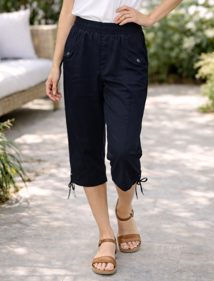 Woman wearing a white t-shirt and black pants standing outdoors with greenery in the background