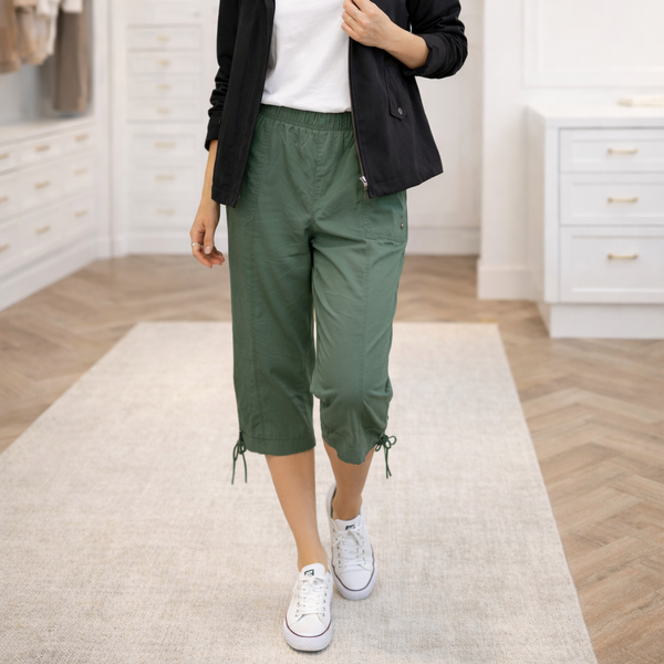 Person wearing green capri pants and white sneakers in a room with wooden floor and white walls.