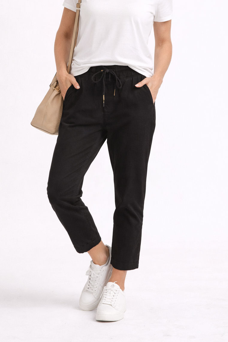 Woman wearing a white t-shirt and black pants with a beige bag on a white background