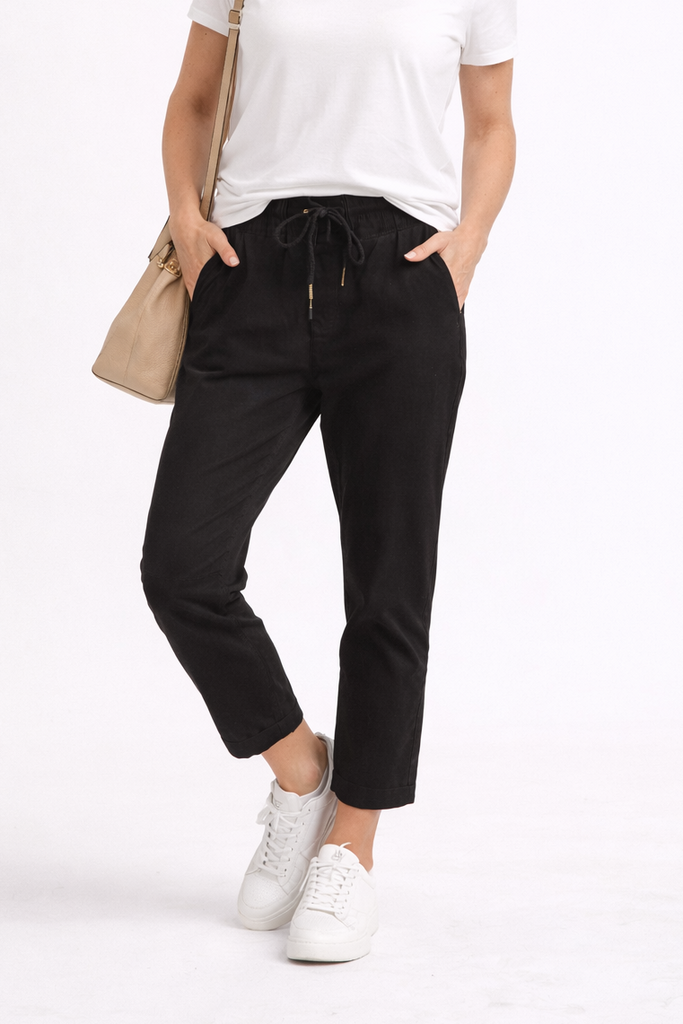 Woman wearing a white t-shirt and black pants with a beige bag on a white background