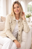 Woman wearing a beige denim jacket sitting on a couch in a bright room.