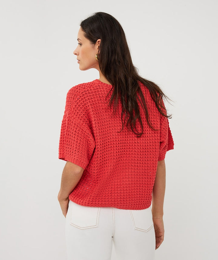 Woman wearing a red textured top and white pants on a light gray background
