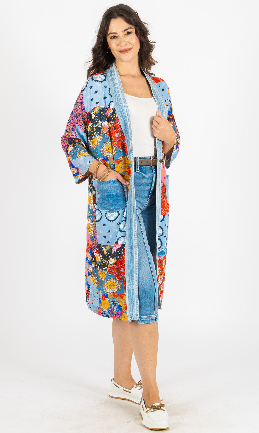 Woman wearing a colorful floral kimono over a white shirt and blue jeans on a white background