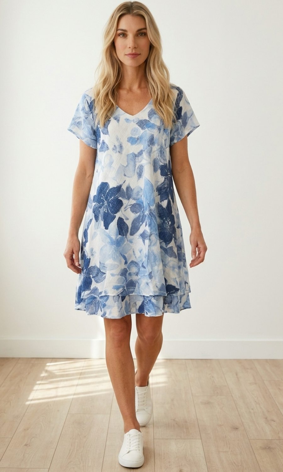 Woman wearing a blue floral dress standing in a well-lit room with wooden floor.