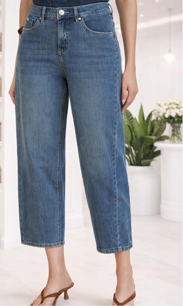 Person wearing blue jeans in a bright indoor setting with plants and shelves.