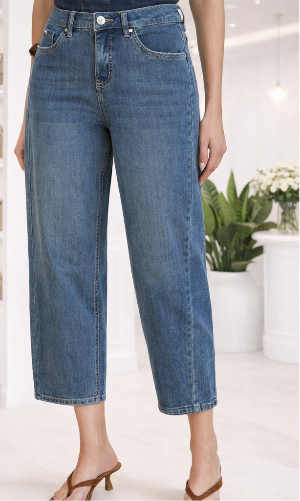 Person wearing blue jeans in a bright indoor setting with plants and shelves.