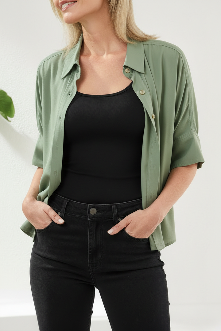 Woman wearing a green shirt over a black top and black pants on a white background