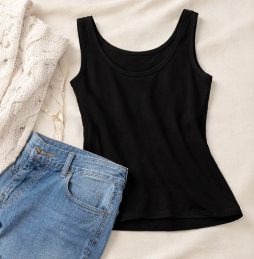 Black tank top and blue jeans on a light beige surface