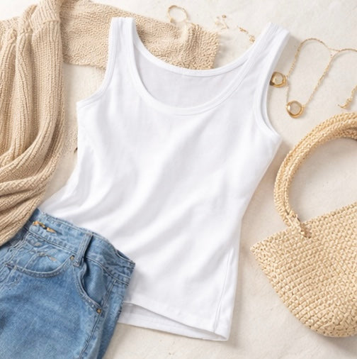 White tank top with blue jeans, beige sweater, and woven bag on a light surface