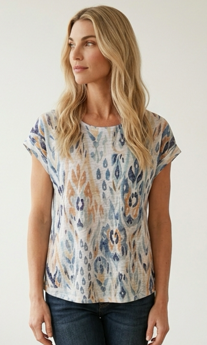 Woman wearing a patterned top and jeans against a plain background