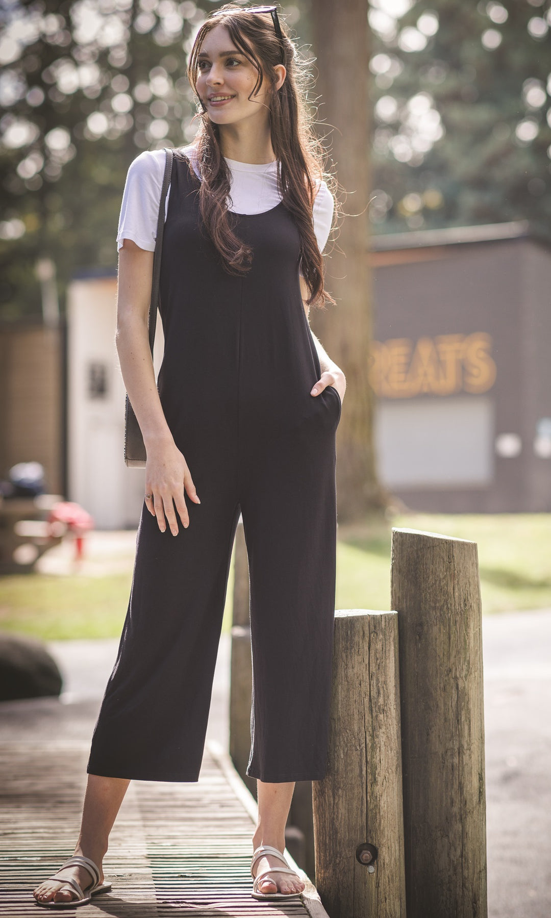 Woman in black jumpsuit standing outdoors near a wooden post