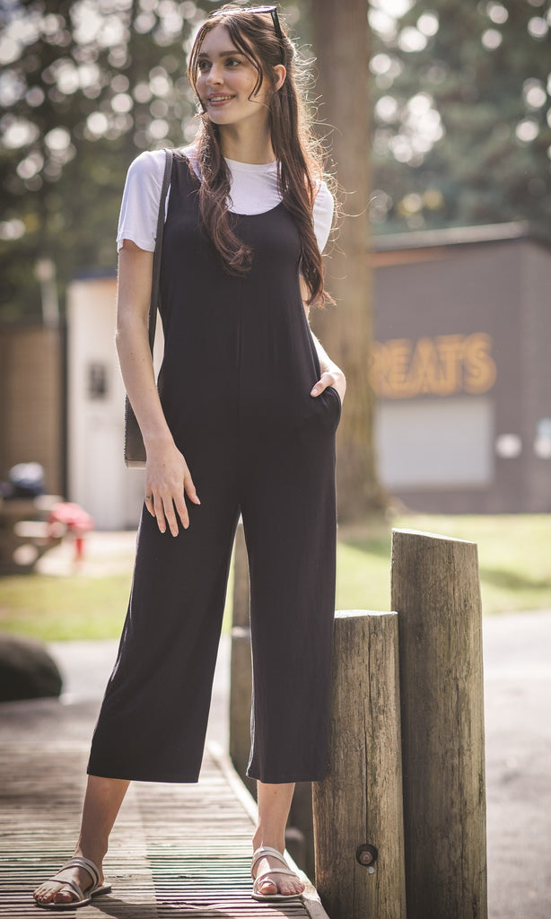 Woman in black jumpsuit standing outdoors near a wooden post