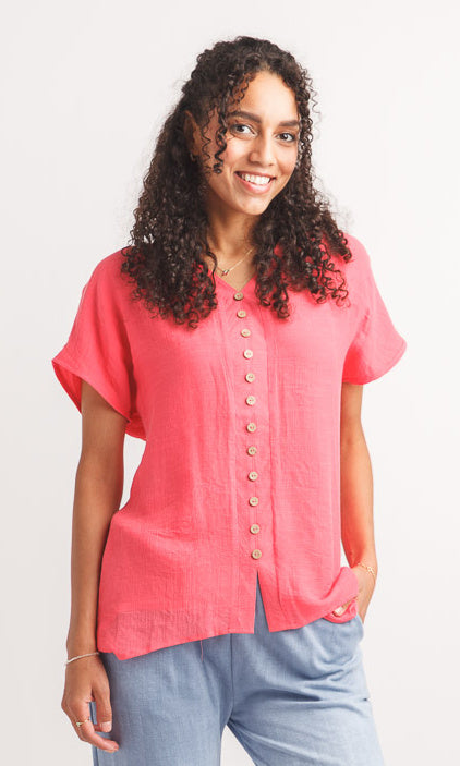 Woman wearing a pink blouse with buttons on a plain background