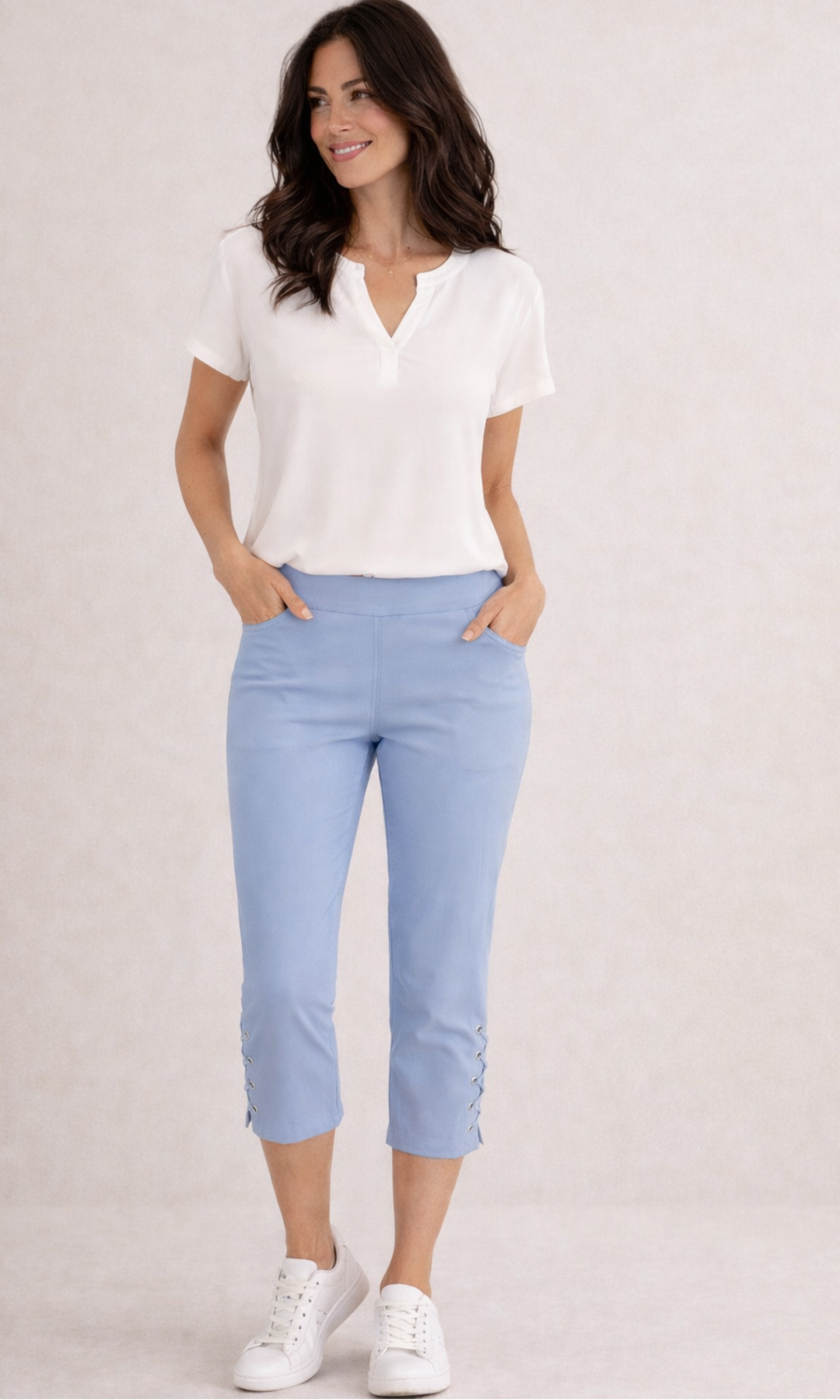 Woman wearing a white blouse and light blue pants on a plain background