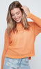 Woman wearing an orange sweater and light blue jeans against a white background