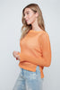 Woman wearing an orange sweater and light blue jeans on a plain background