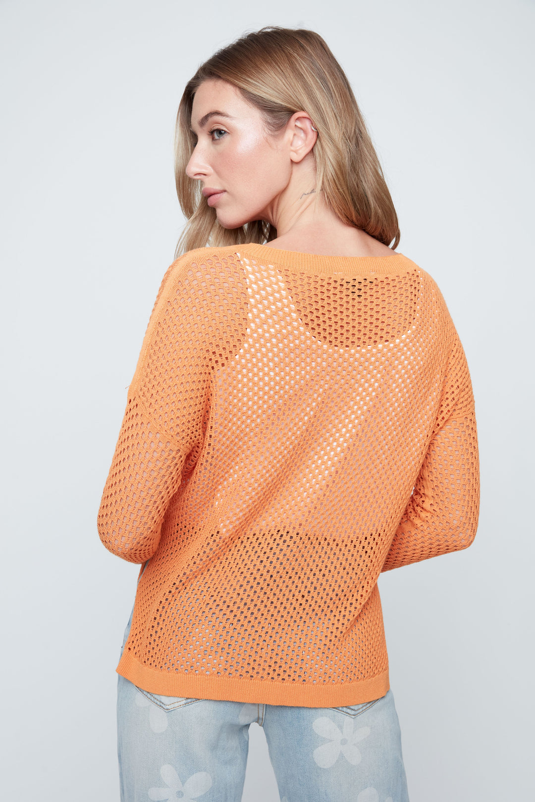 Woman wearing an orange knitted sweater against a plain background