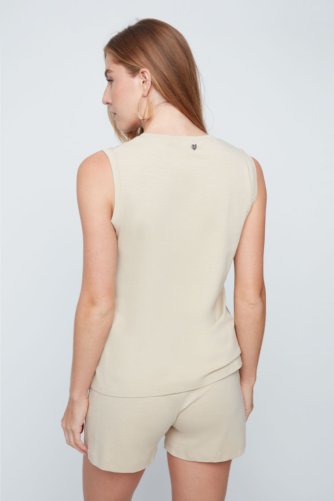 Woman wearing a beige sleeveless top and shorts set on a light gray background