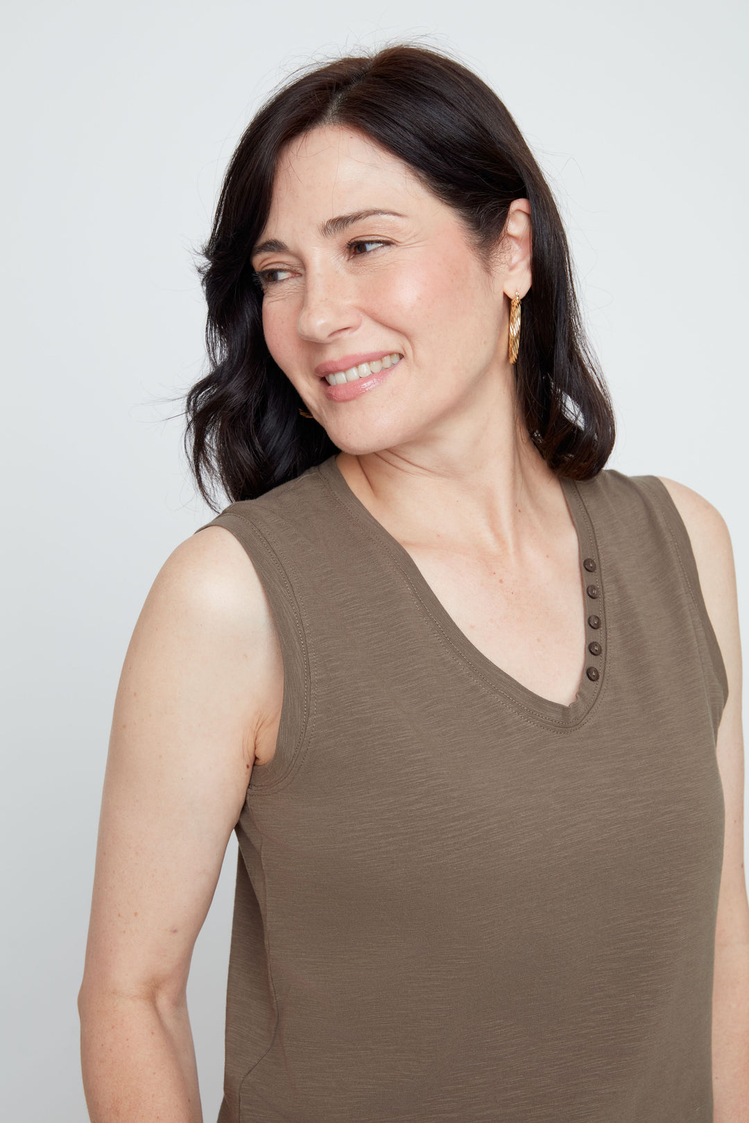 Woman wearing a brown sleeveless top against a plain background