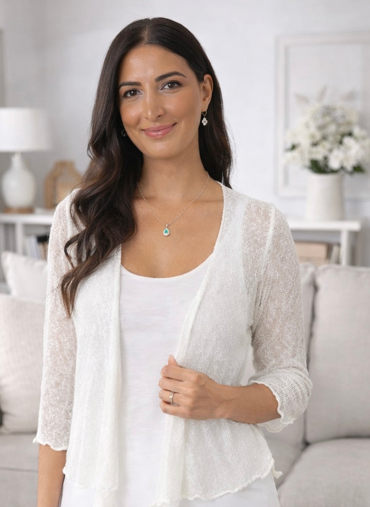 Woman wearing a light cardigan over a white top in a bright room.