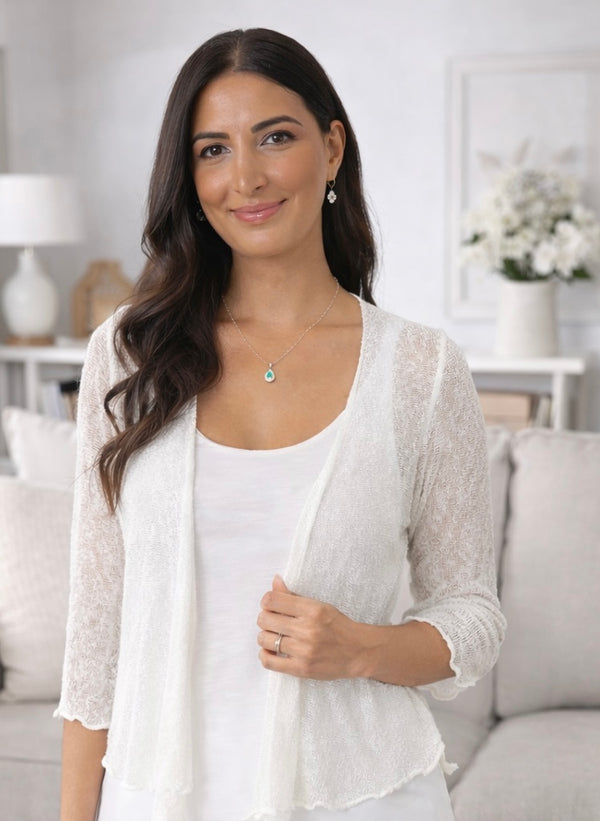 Woman wearing a light cardigan over a white top in a bright room.
