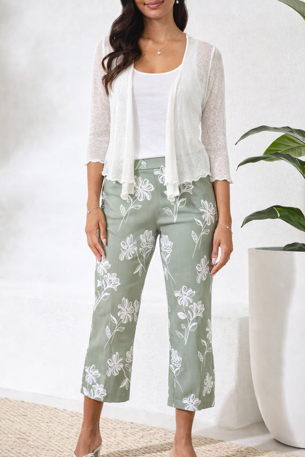 Woman wearing a white cardigan, white top, and green floral pants against a white background.