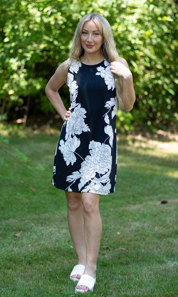 Woman wearing a black dress with white floral patterns outdoors.