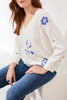 Woman wearing a white sweater with floral embroidery sitting on a white surface.