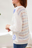 Person wearing a white sweater with colorful stripes and blue floral designs.