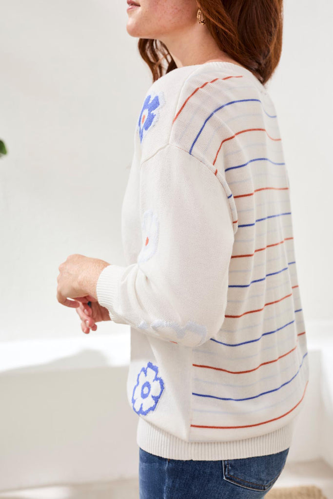 Person wearing a white sweater with colorful stripes and blue floral designs.