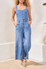 Woman wearing a denim jumpsuit standing in a room with a neutral background