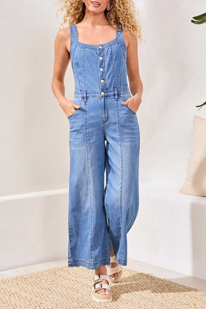 Woman wearing a denim jumpsuit standing in a room with a neutral background