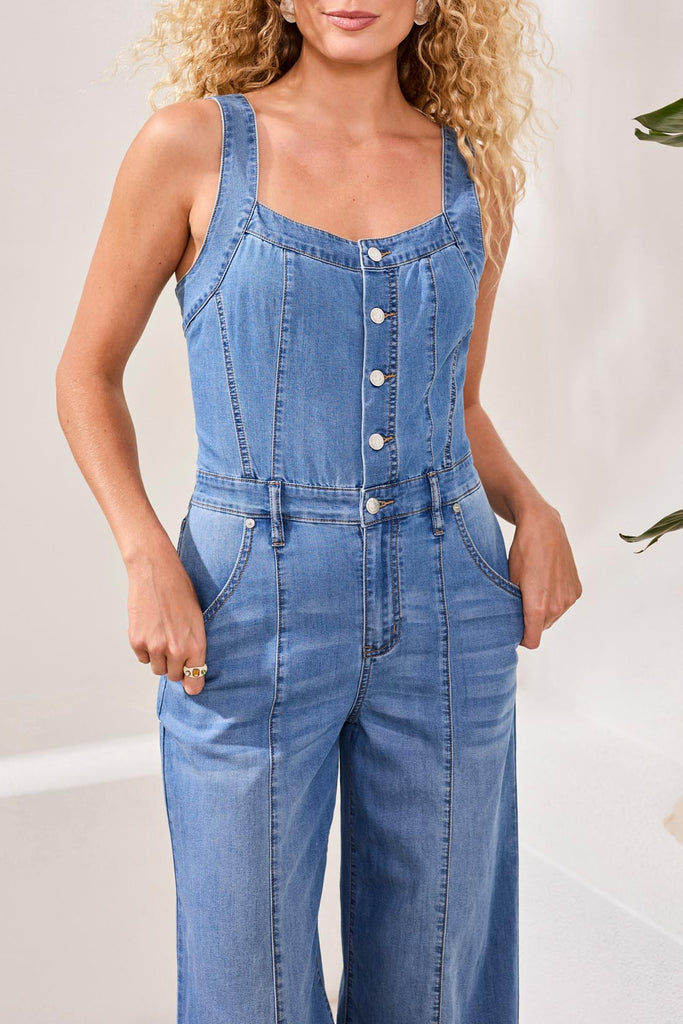 Woman wearing a blue denim jumpsuit against a plain background