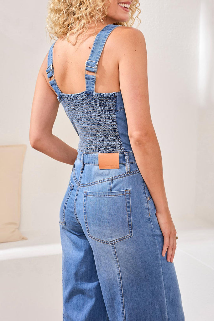 Person wearing a denim jumpsuit with a plain background
