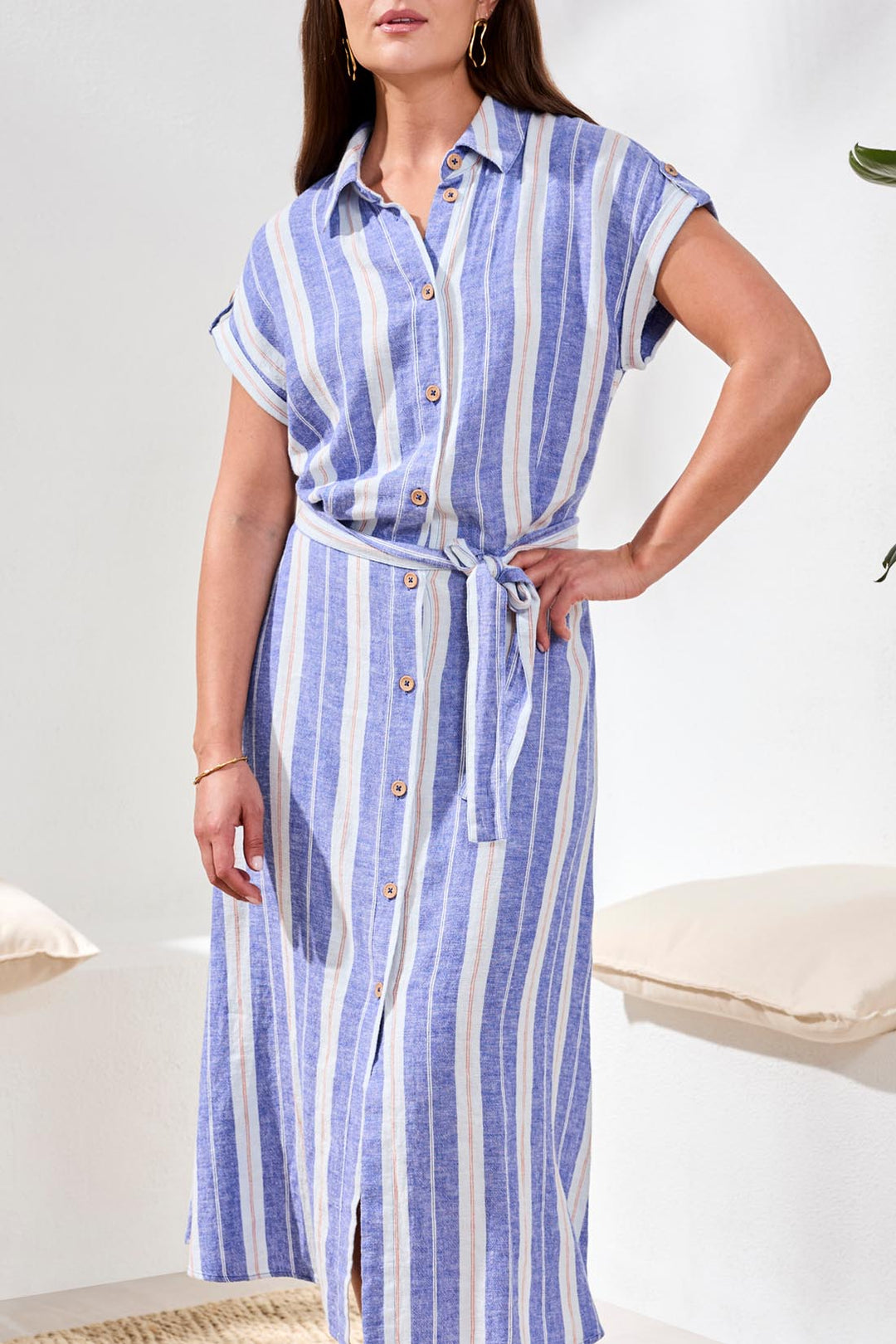 Woman wearing a blue and white striped dress with a belt in a minimal indoor setting.