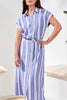 Woman wearing a blue and white striped dress with a belt in a minimal indoor setting.
