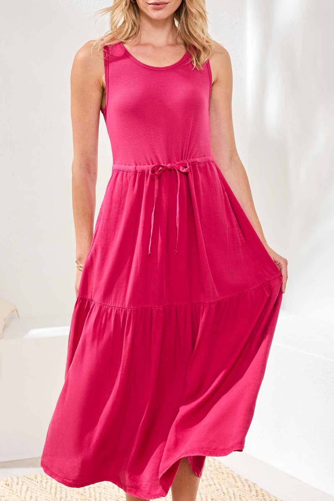 Woman wearing a bright pink sleeveless dress against a white background