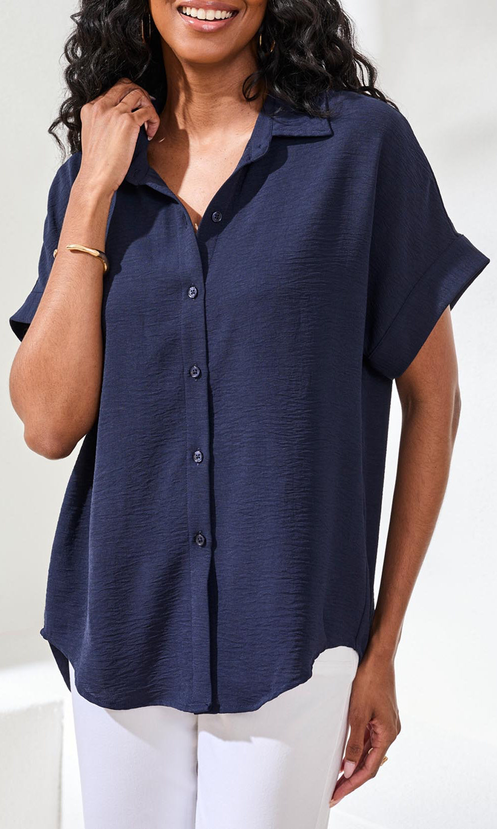 Woman wearing a navy blue button-up shirt with white pants on a white background