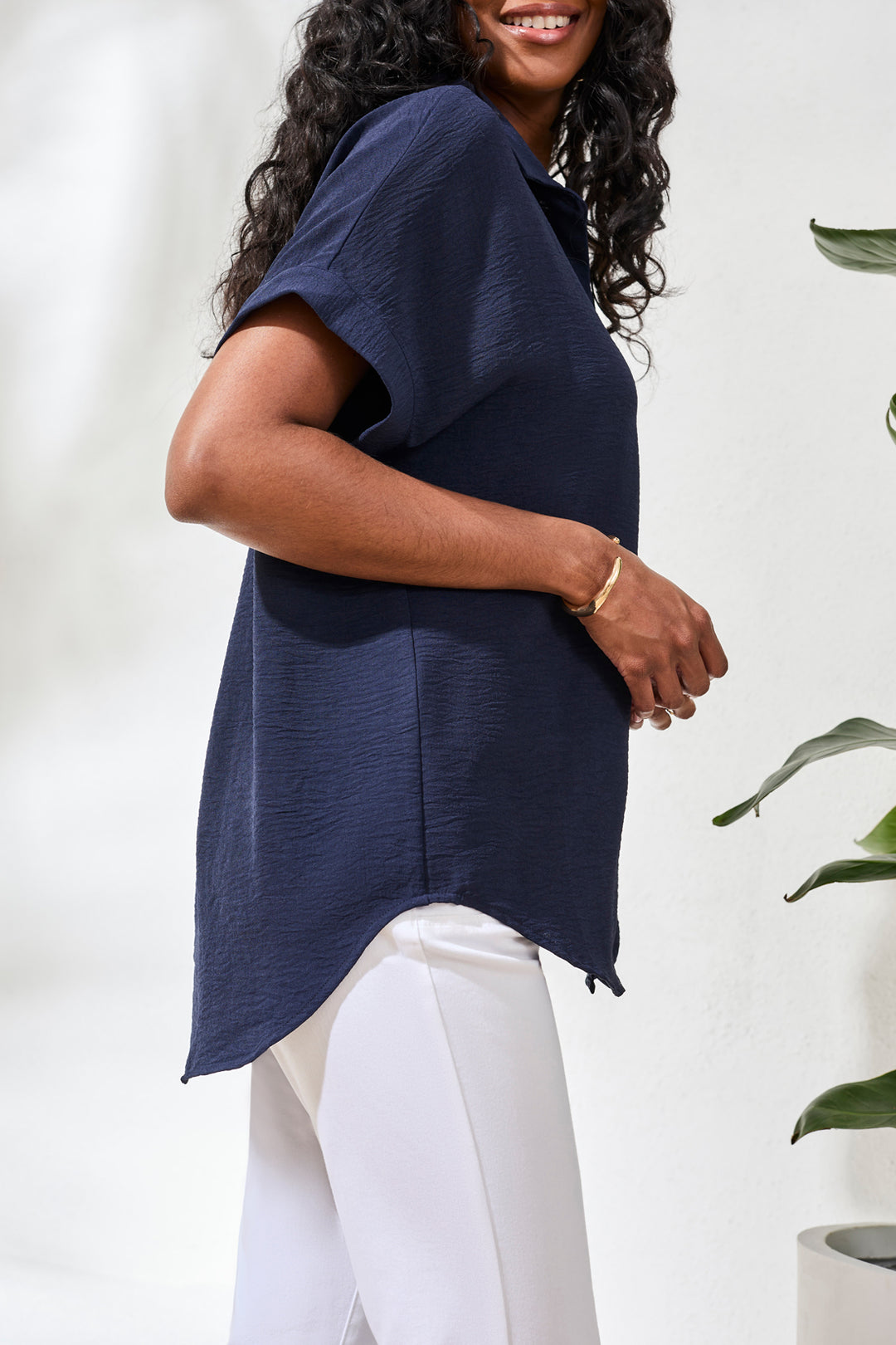 Woman wearing a navy blue top and white pants against a white background