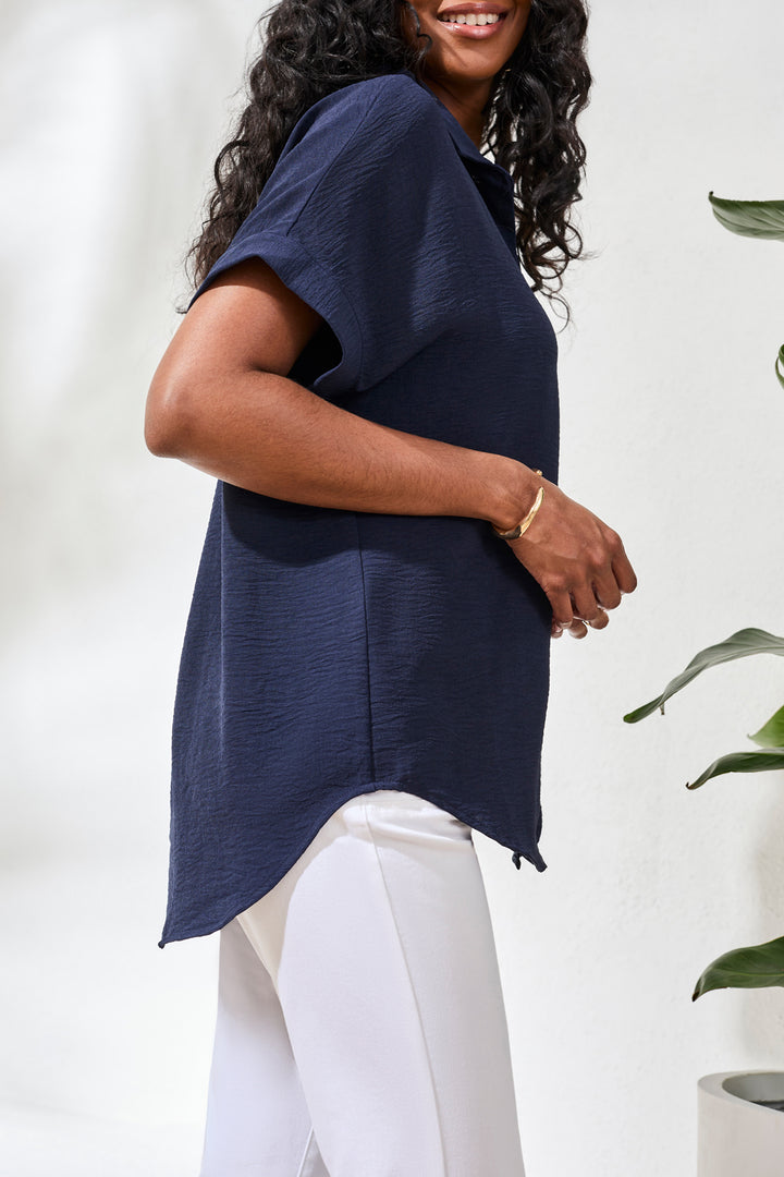 Woman wearing a navy blue top and white pants against a white background