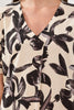Close-up of a person wearing a blouse with black floral pattern on beige background