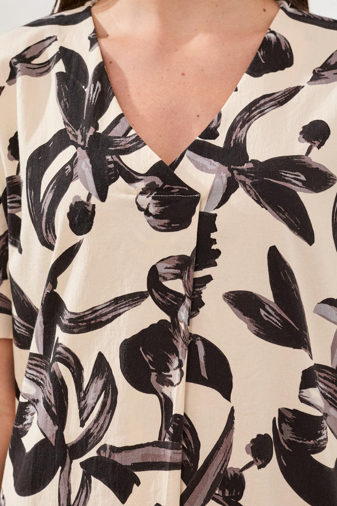Close-up of a person wearing a blouse with black floral pattern on beige background