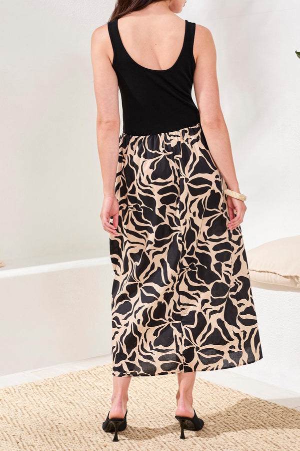 Woman wearing a black tank top and patterned skirt on a plain background